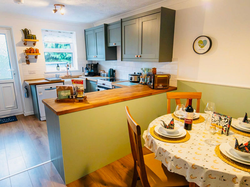 Fully equipped kitchen with sage green cabinets and dining table for four