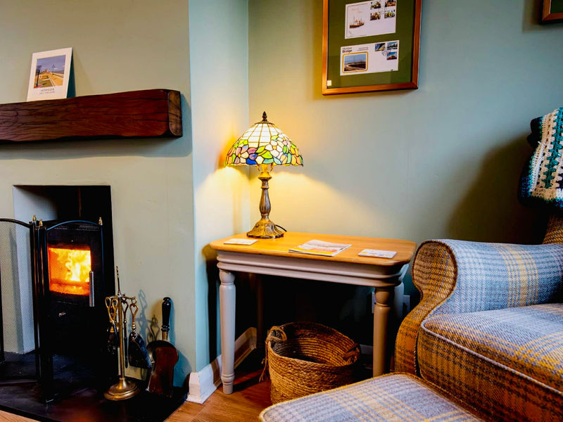 Cosy lounge with lit wood-burning stove and comfortable armchair